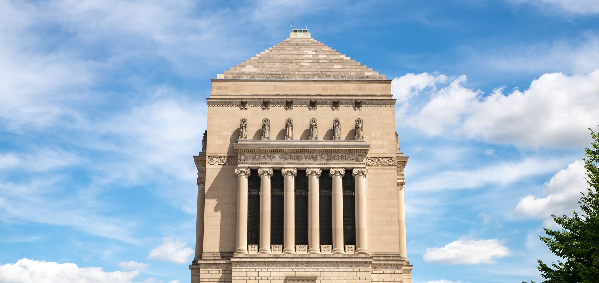 Stone neoclassical building facade with tall columns against a blue sky and clouds
