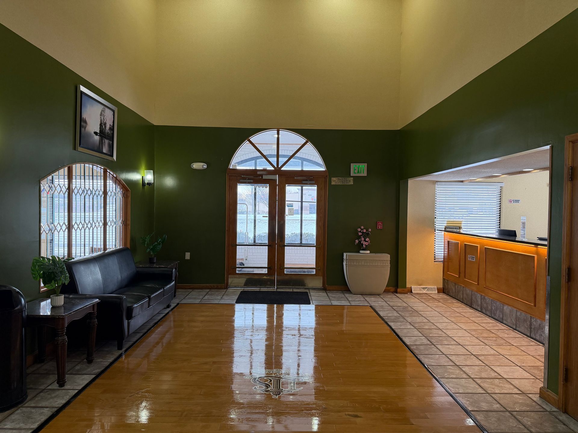 Lobby with dark green walls, wood floor, glass doors, and a front desk.