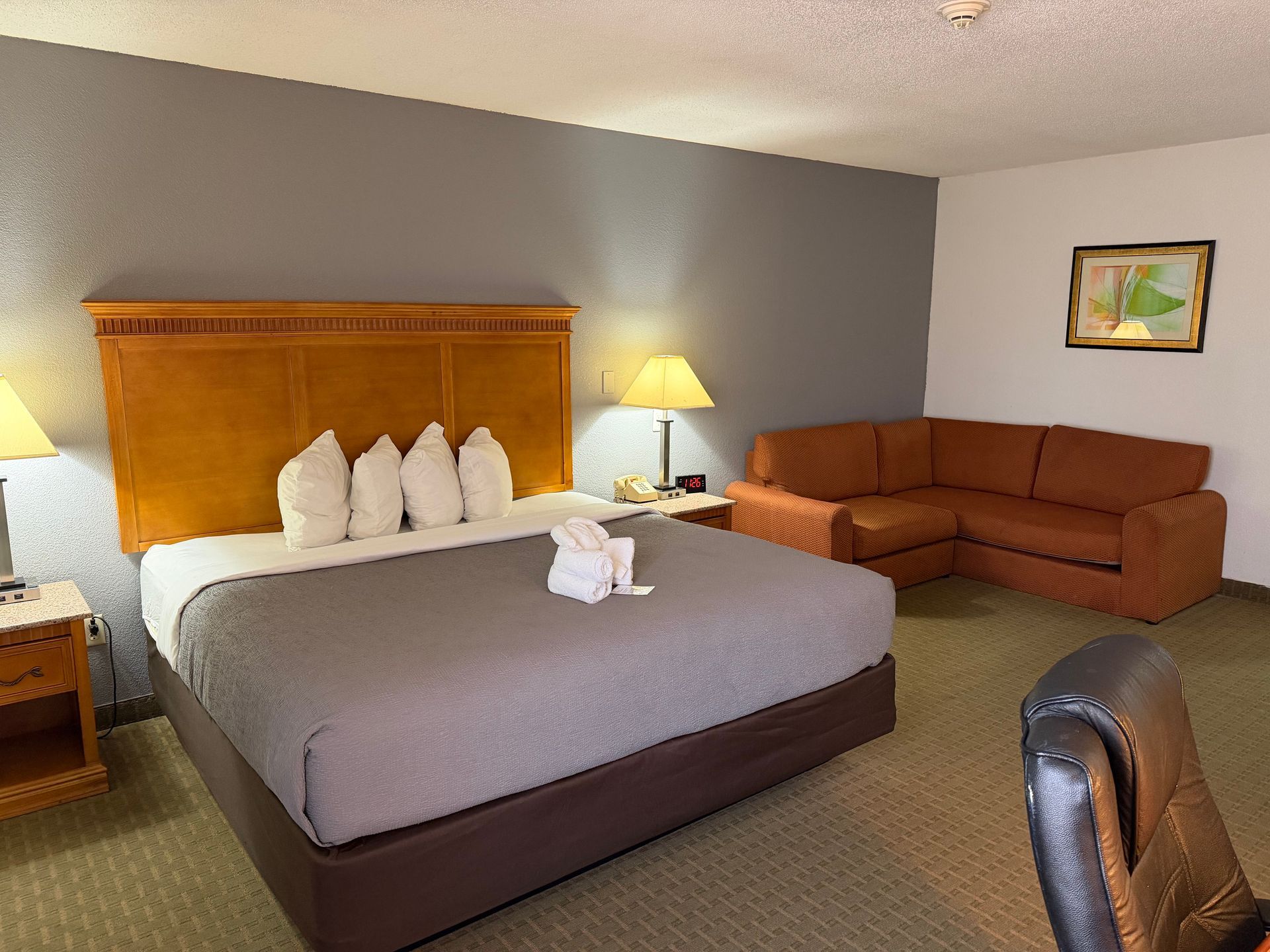 Hotel room with king bed, sofa, desk, and bedside table with lamp.