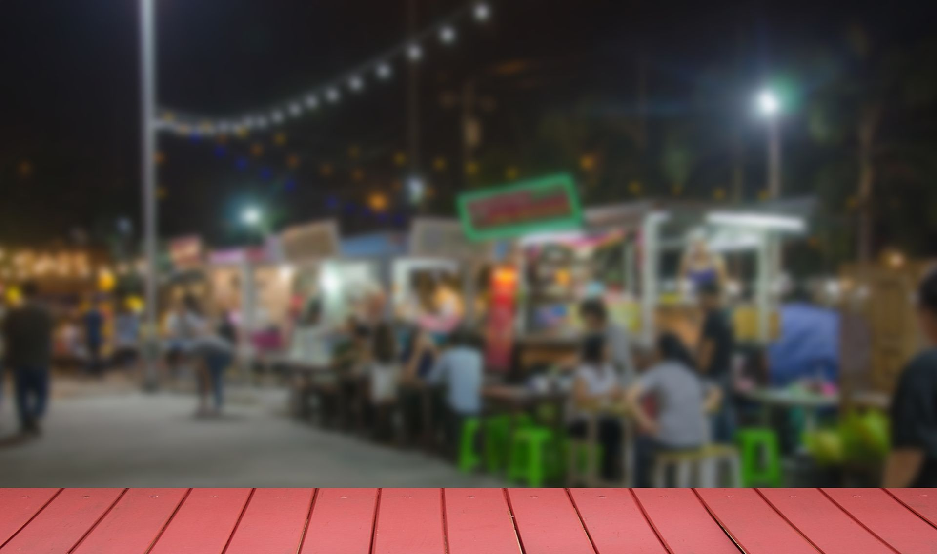 Night market with food stalls, string lights, and people seated at tables outdoors.