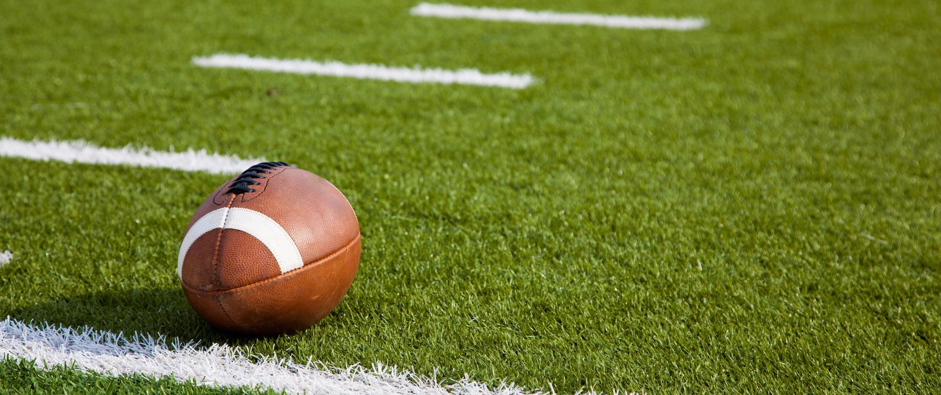 Football resting on green turf near a white sideline stripe