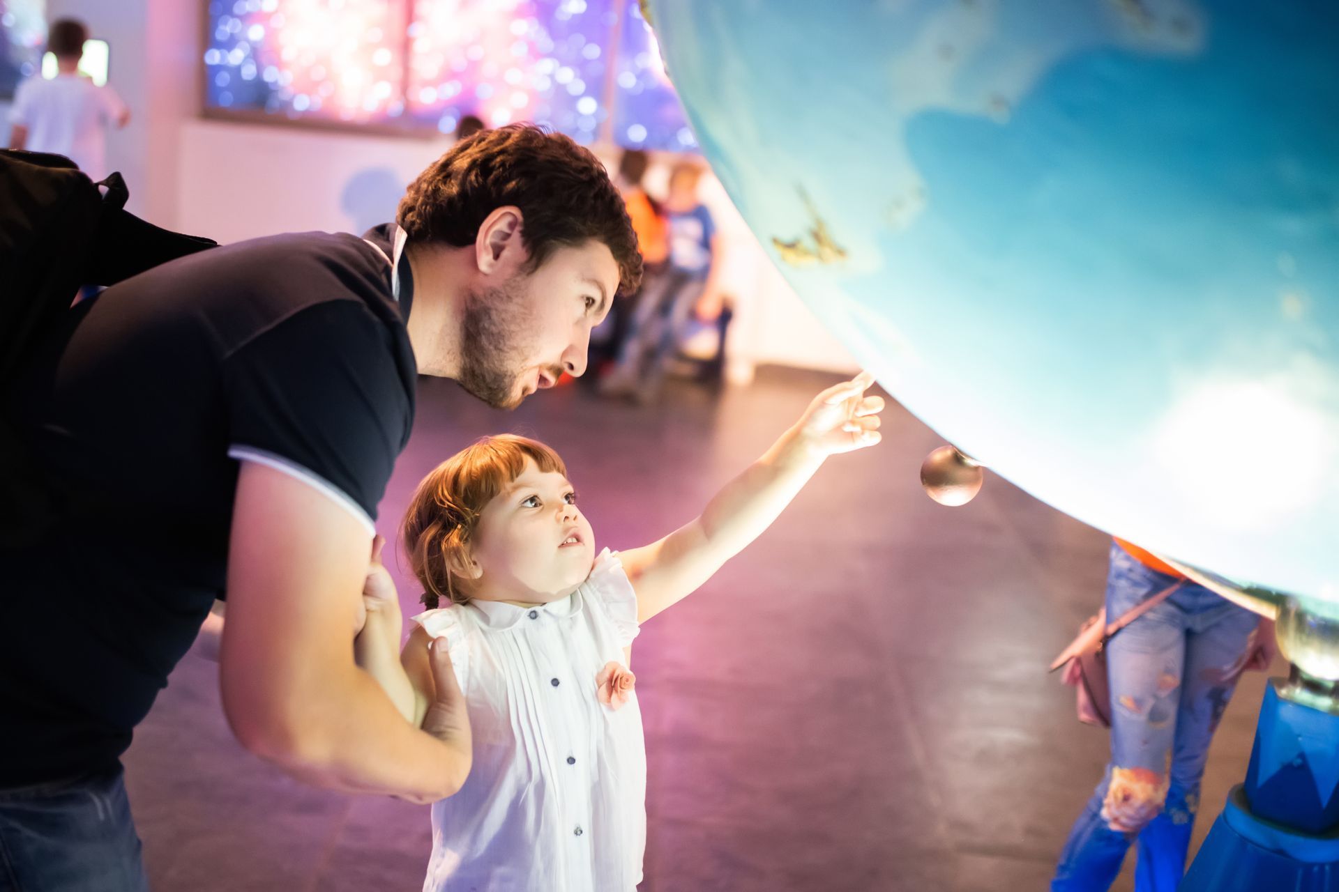 Man and child reaching toward a glowing blue globe in a colorful interactive exhibit