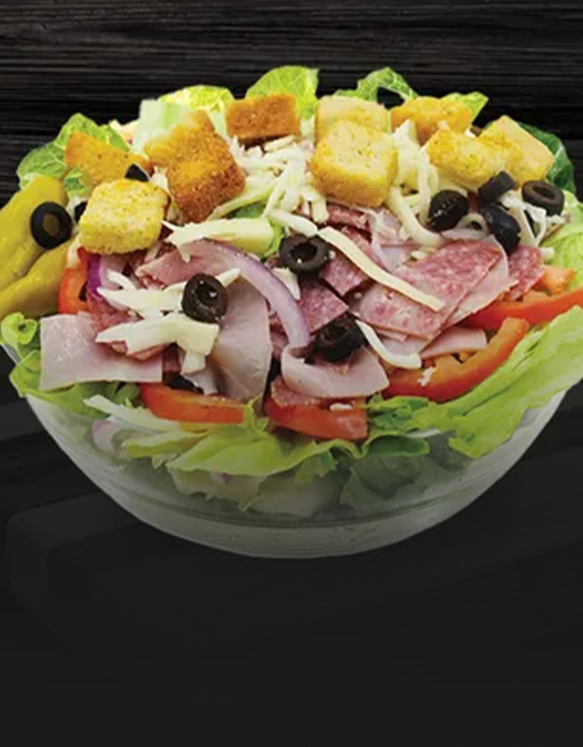 Close-up of a mixed salad with grilled chicken, lettuce, and crunchy croutons on a black plate