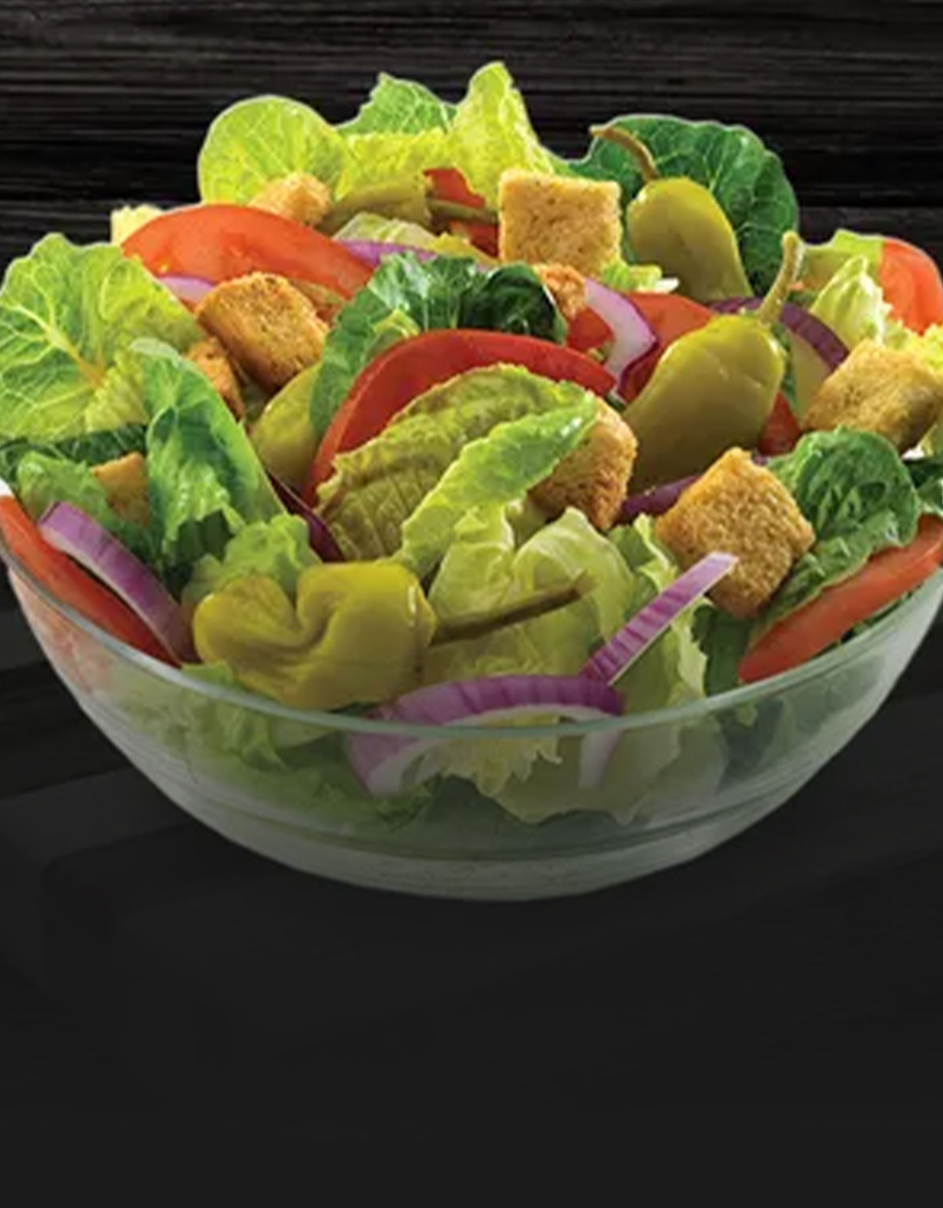 Close-up of a fresh salad served on a black plate with grilled chicken and dressing