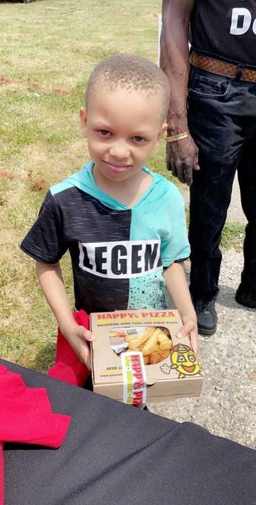 A young boy wearing a legend shirt is holding a box of french fries.