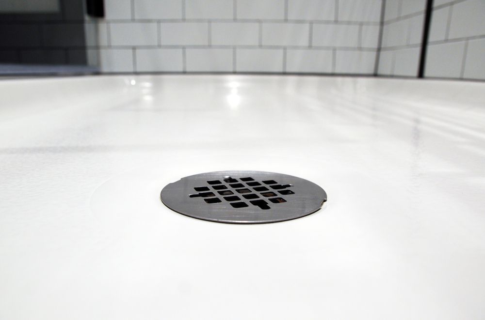 White shower floor with a round metal drain in the center