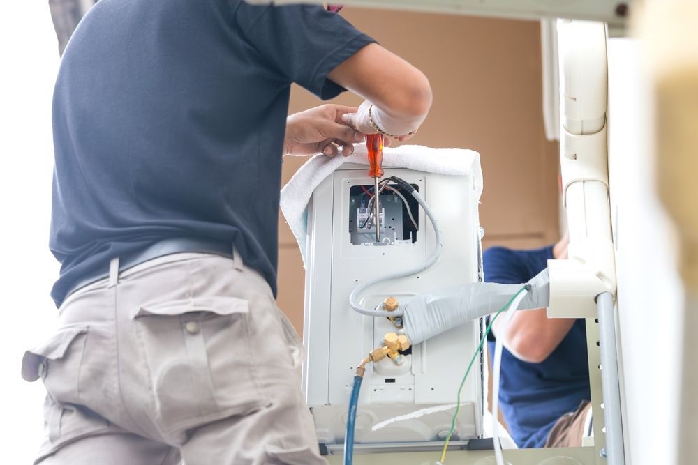 Person inspecting a white utility unit beside a wall outdoors