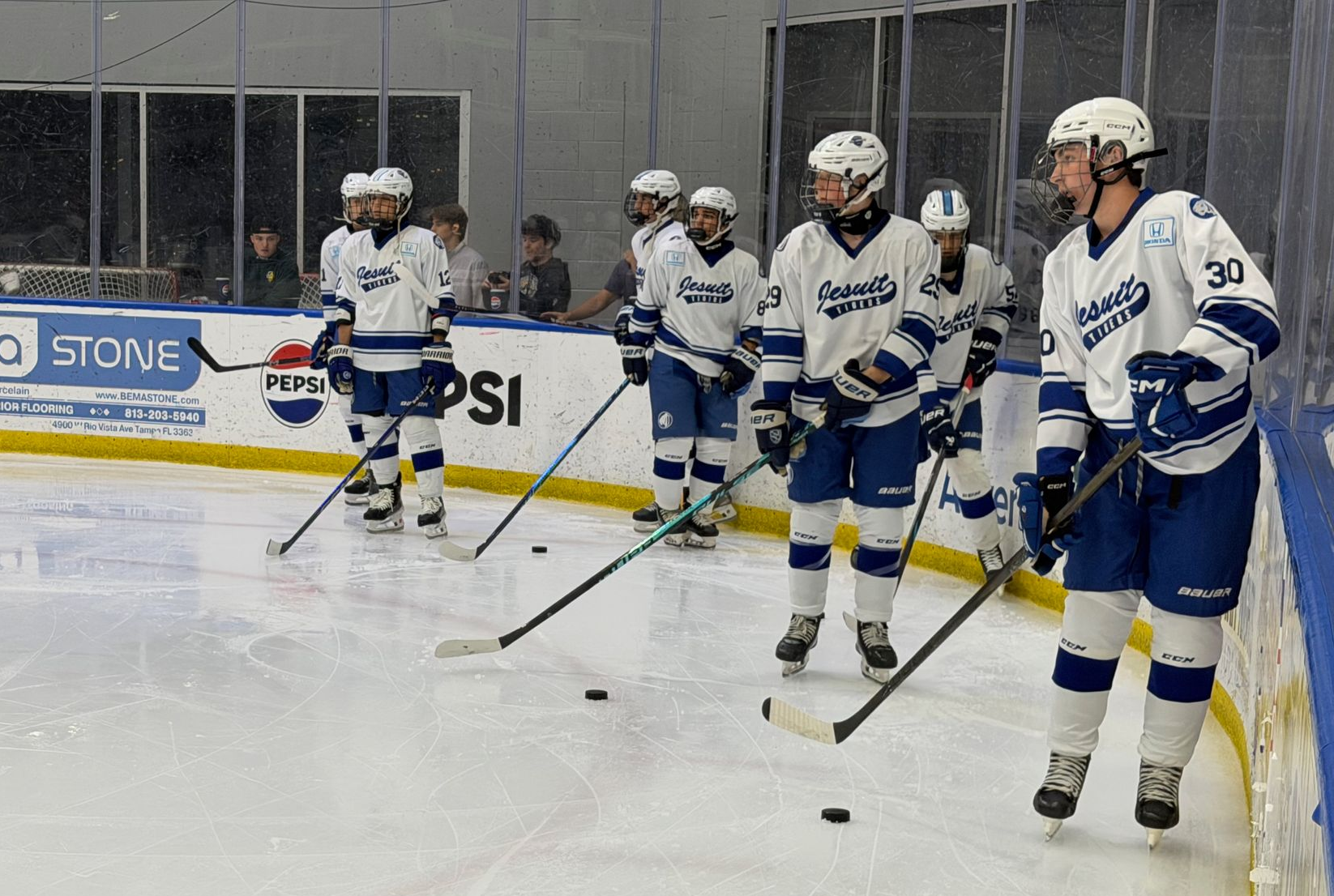 Hockey players in white and blue uniforms lined up on the ice during warmup drills