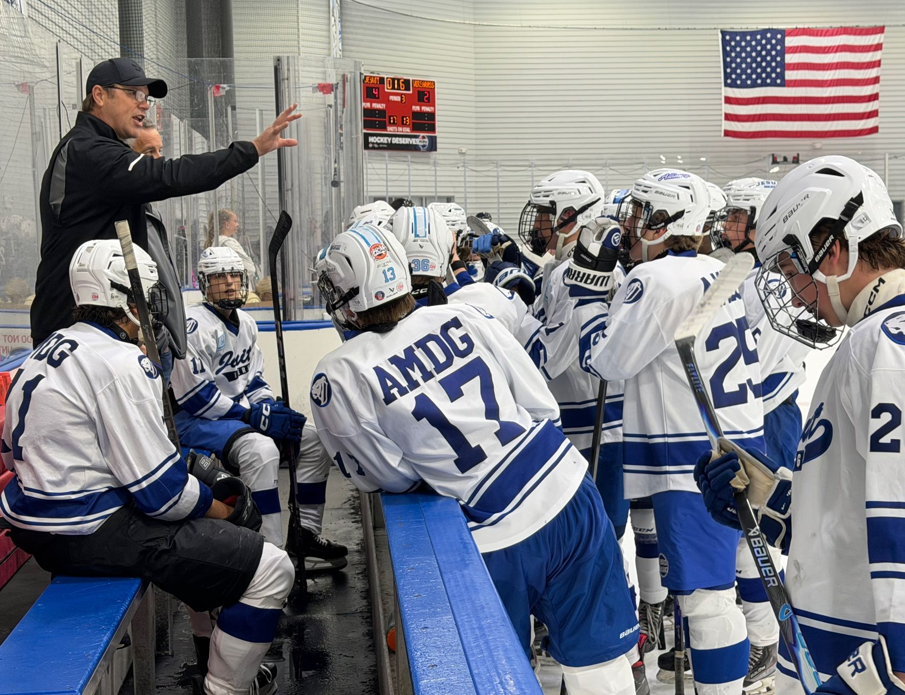 Youth hockey team huddles on bench while coach gives instructions, American flag in background