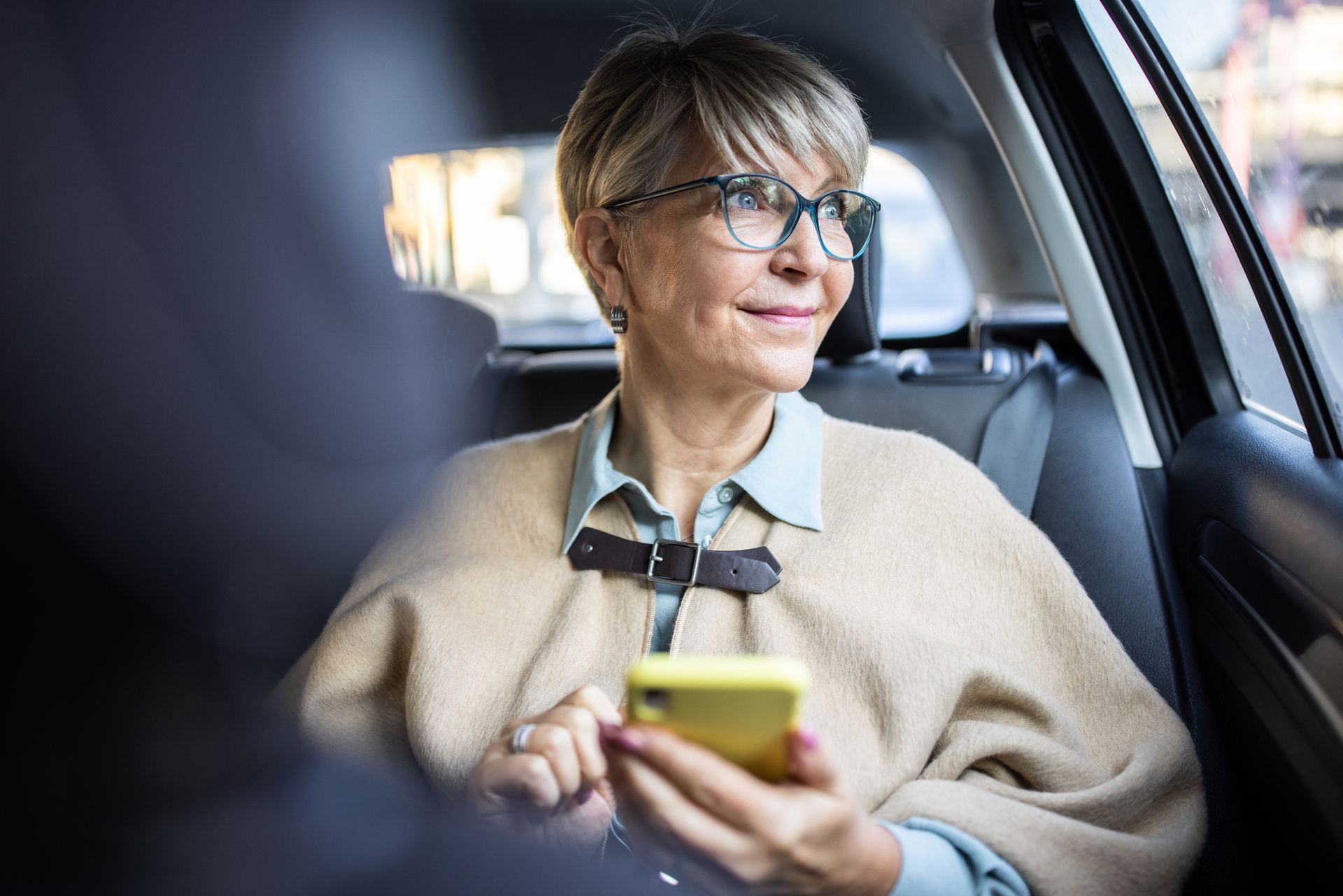 An older woman is sitting in the back seat of a car using a cell phone.