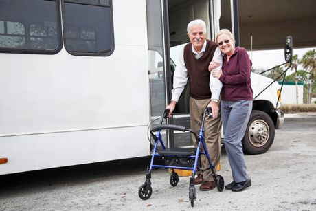An elderly couple with a walker standing next to a bus.