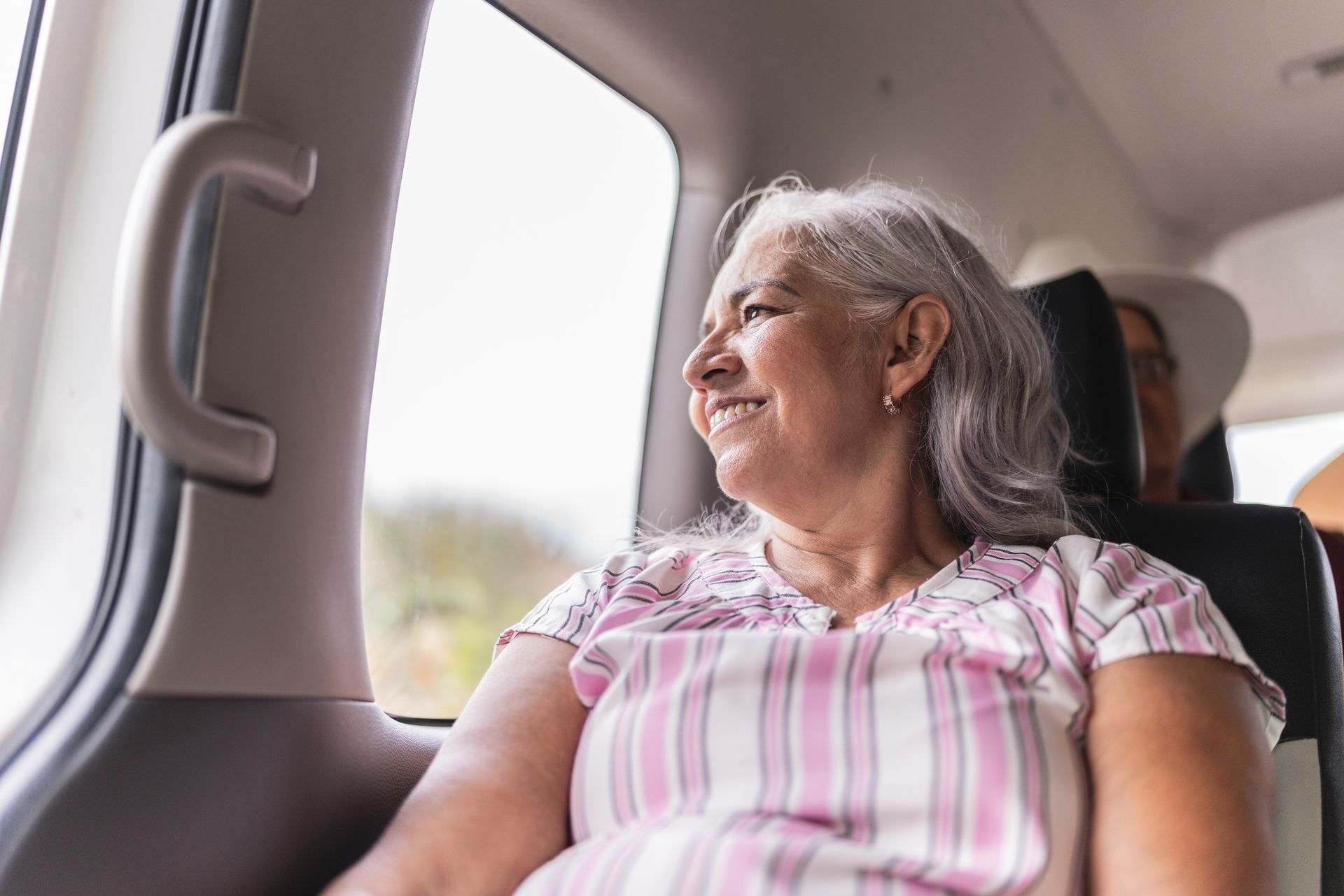 An elderly woman is sitting in the back seat of a car looking out the window. An elderly woman is sitting in the back seat of a car looking out the window.