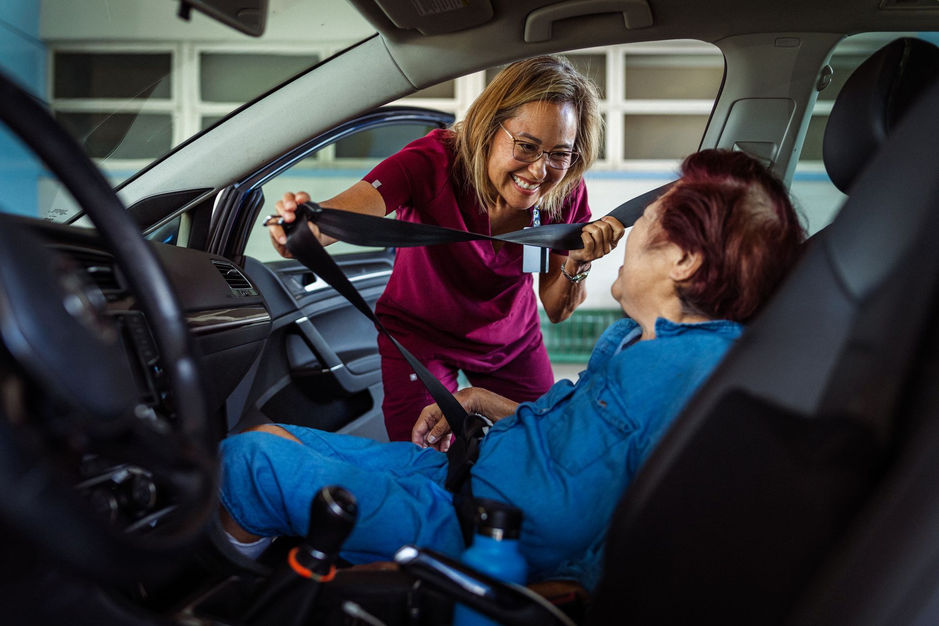 A nurse is helping an elderly woman put on a seat belt in a car.