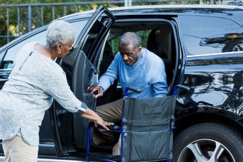 A woman is helping a man in a wheelchair get out of a car.