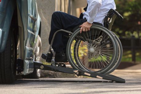 A man in a wheelchair is using a ramp to get into a car.