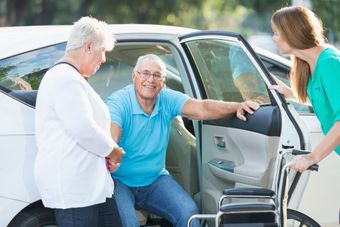 A woman is helping an elderly man in a wheelchair get out of a car. A woman is helping an elderly man in a wheelchair get out of a car.