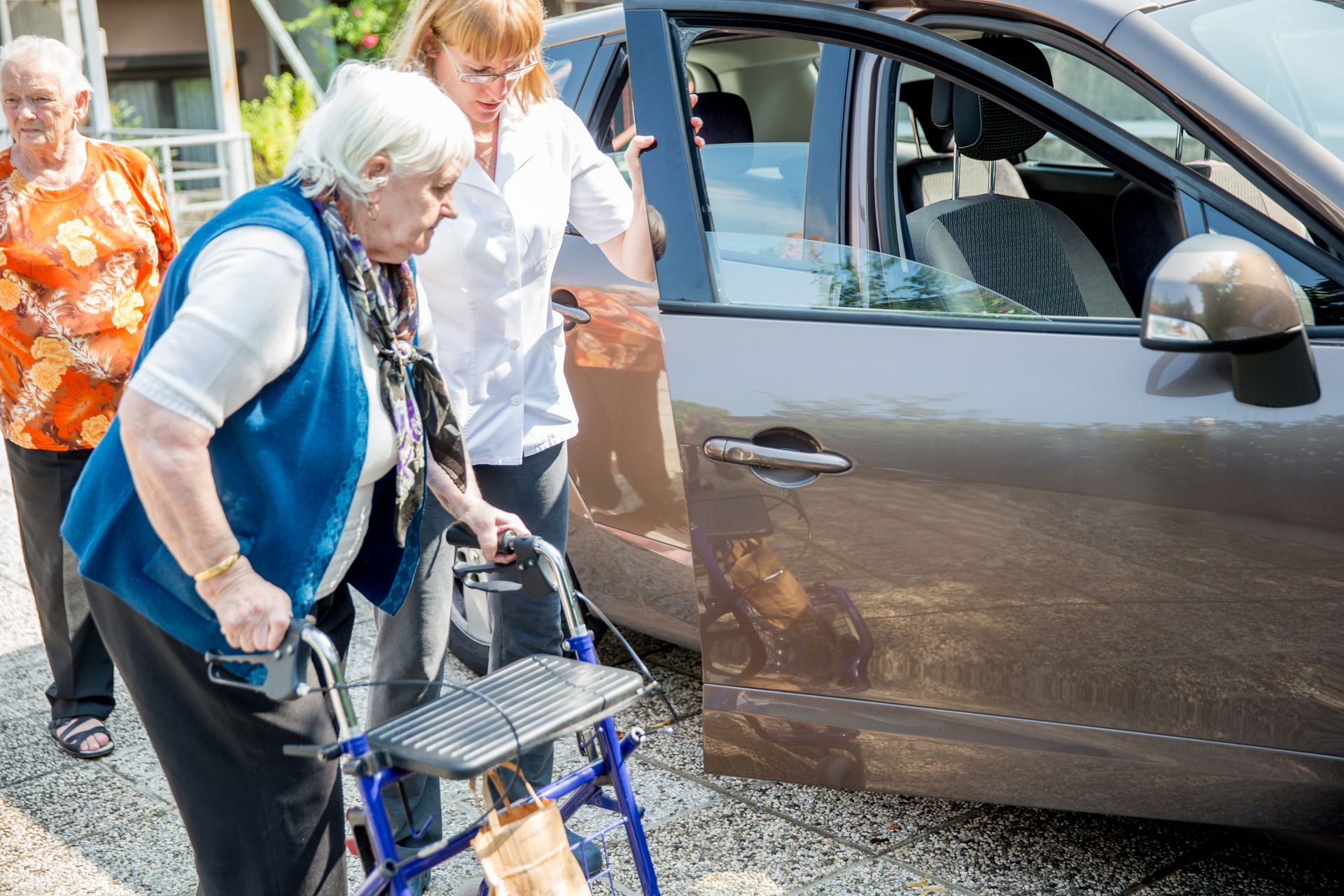 An elderly woman with a walker is getting into a car.