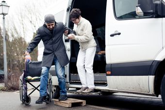 A woman is helping a man in a wheelchair get out of a van.