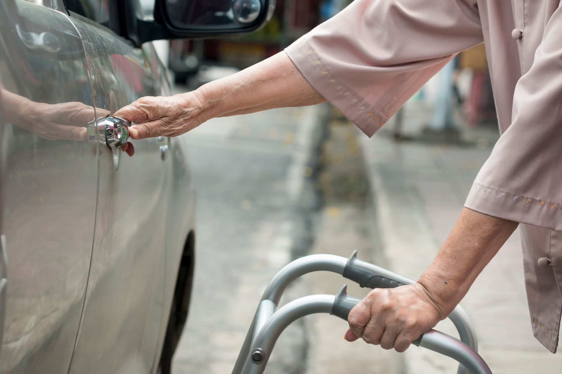 An elderly woman is using a walker to get into a car.