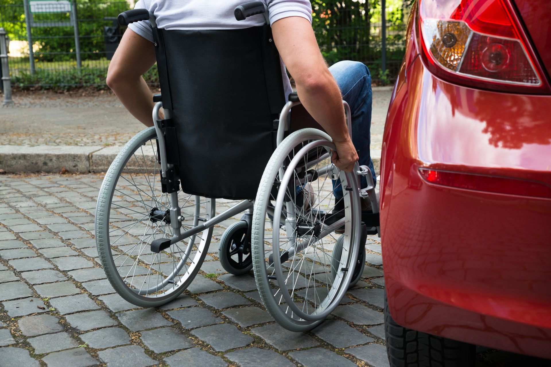 A person in a wheelchair is sitting next to a red car.