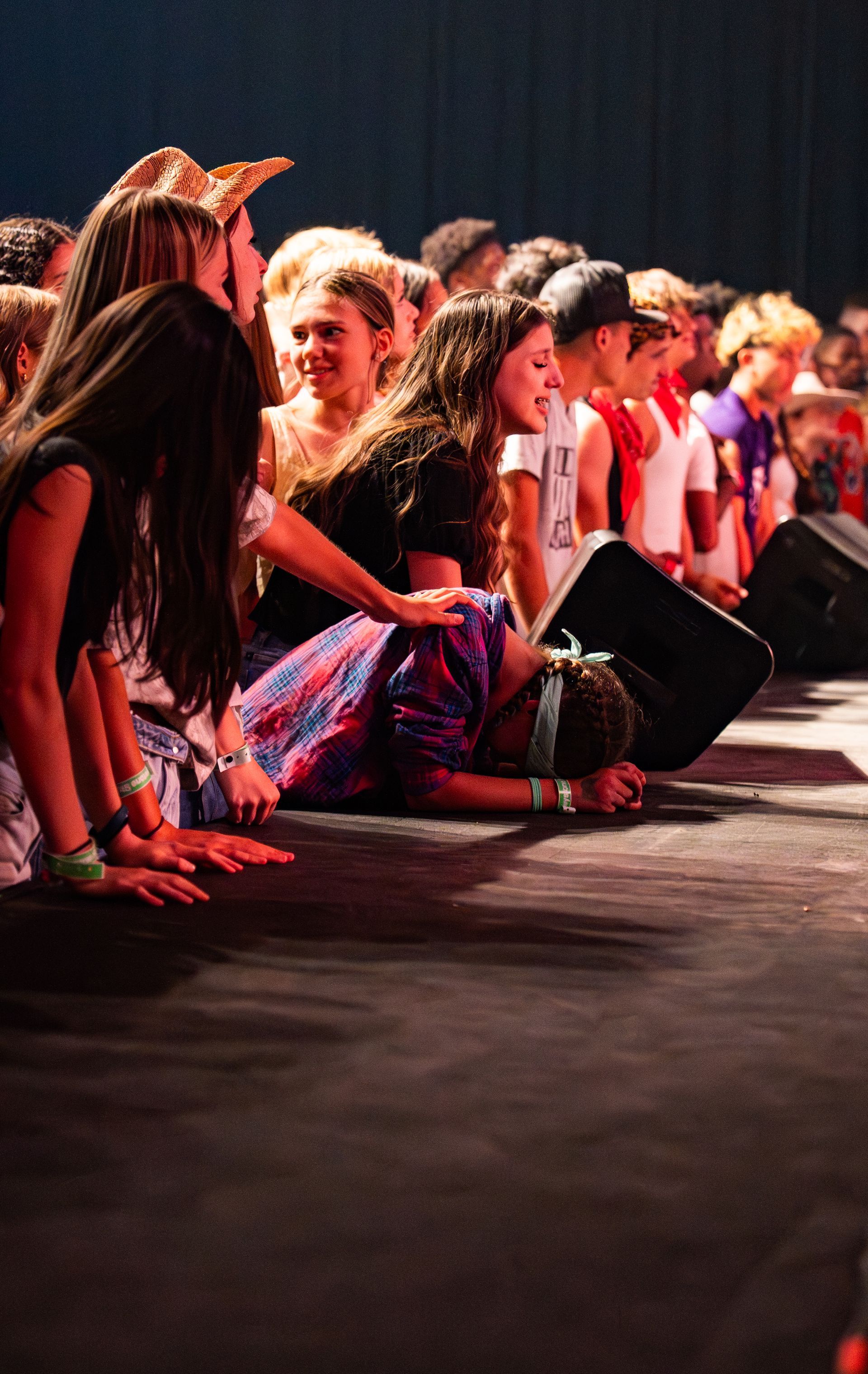 People seated in a row on a dark stage, watching an event under warm red lighting.