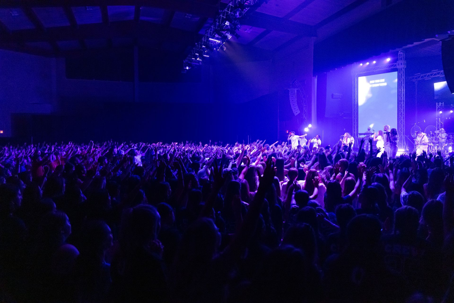 Crowd at a concert in a dark venue, lit by blue and purple stage lights
