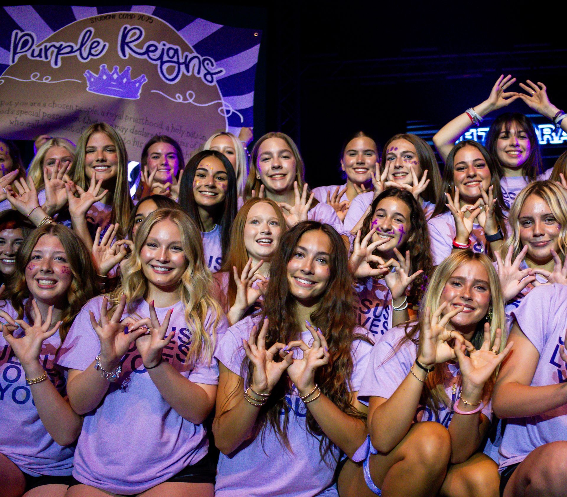 Purple-clad group posing and smiling in front of a “Purple Reign” backdrop at a celebratory event