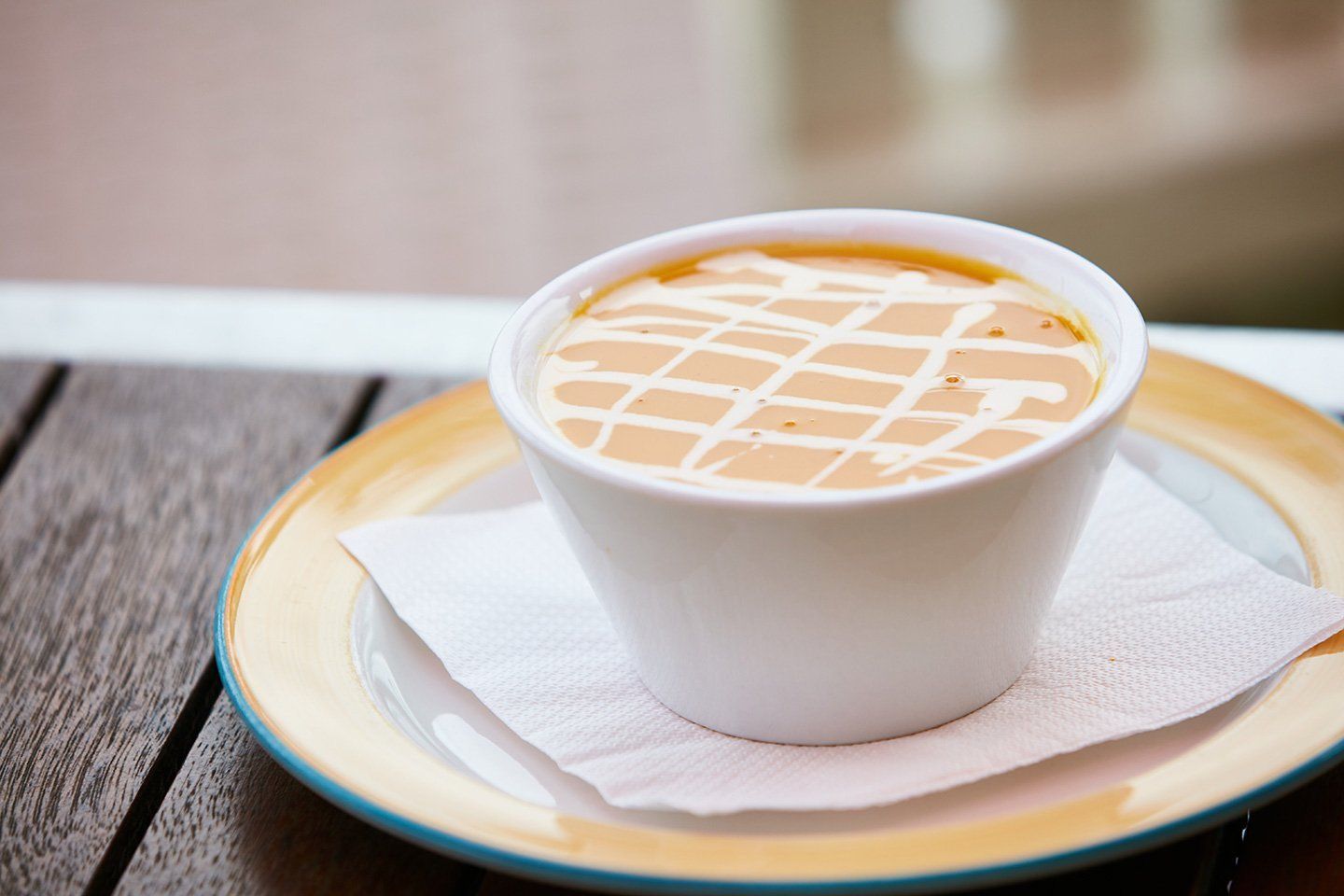 A cup of soup is on a plate on a wooden table.