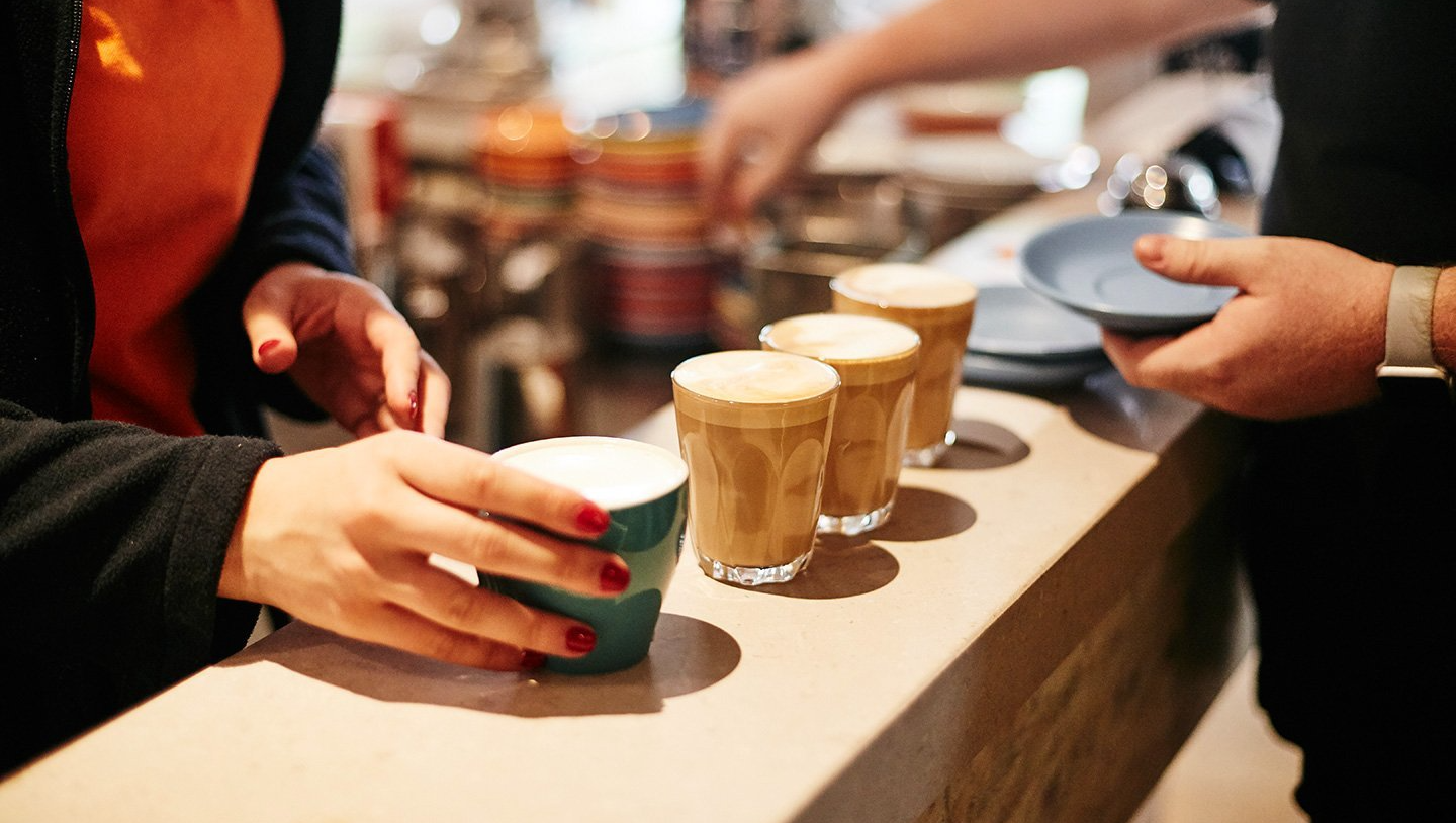 A woman is taking a cup of coffee from a barista.