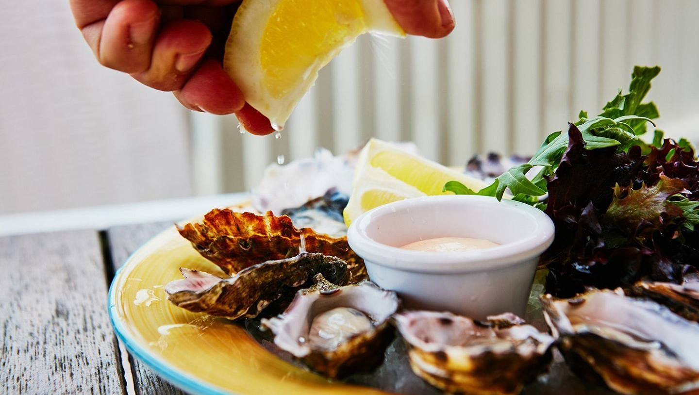 A person is squeezing lemon juice on a plate of oysters.
