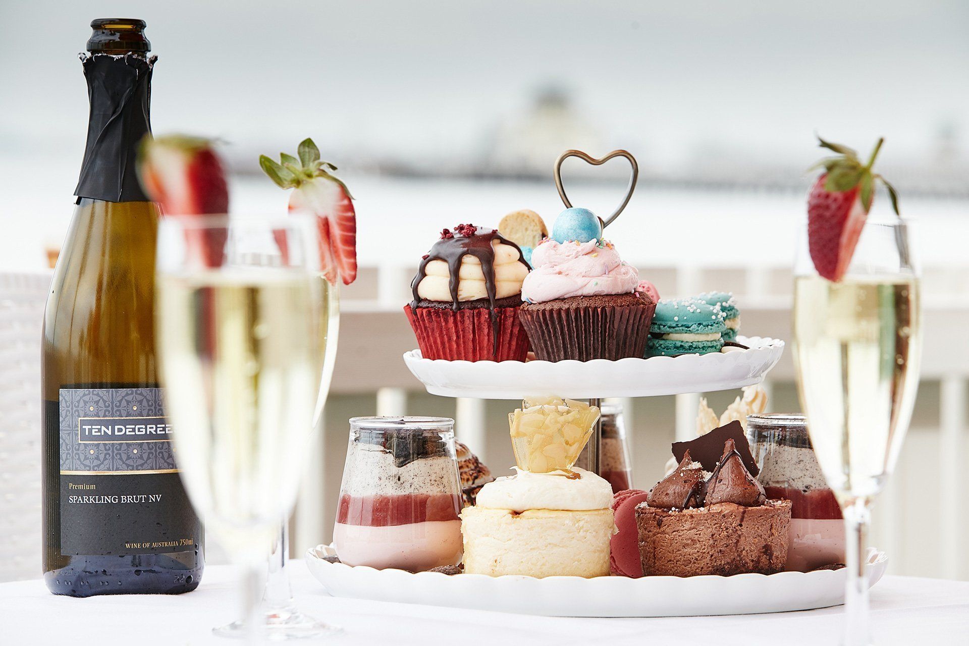 A bottle of champagne is sitting next to a cake stand with cupcakes on it.