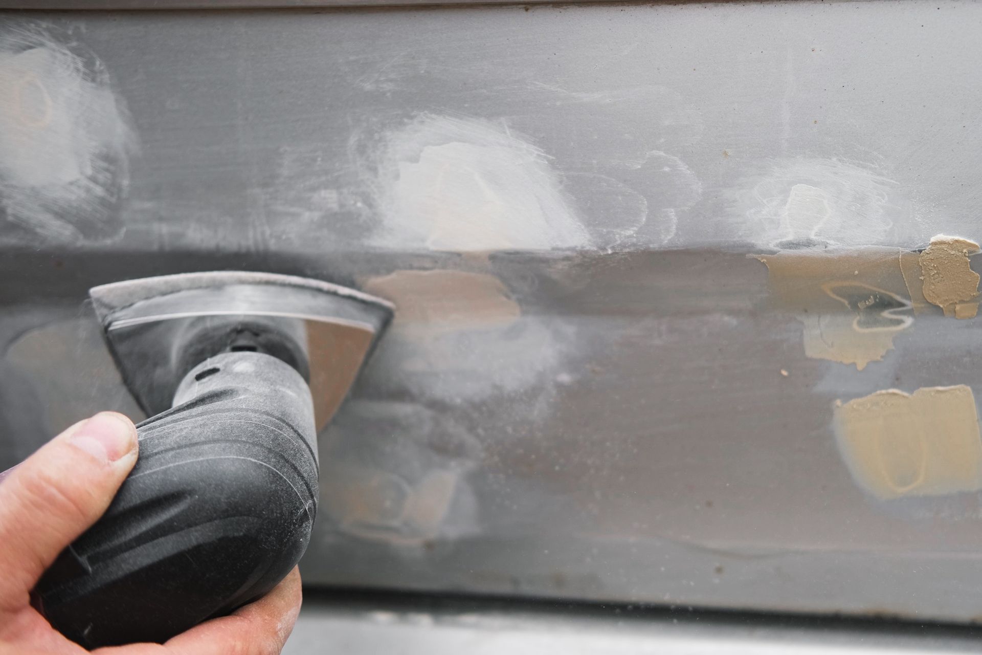 Hand sanding a gray car panel with body filler patches visible