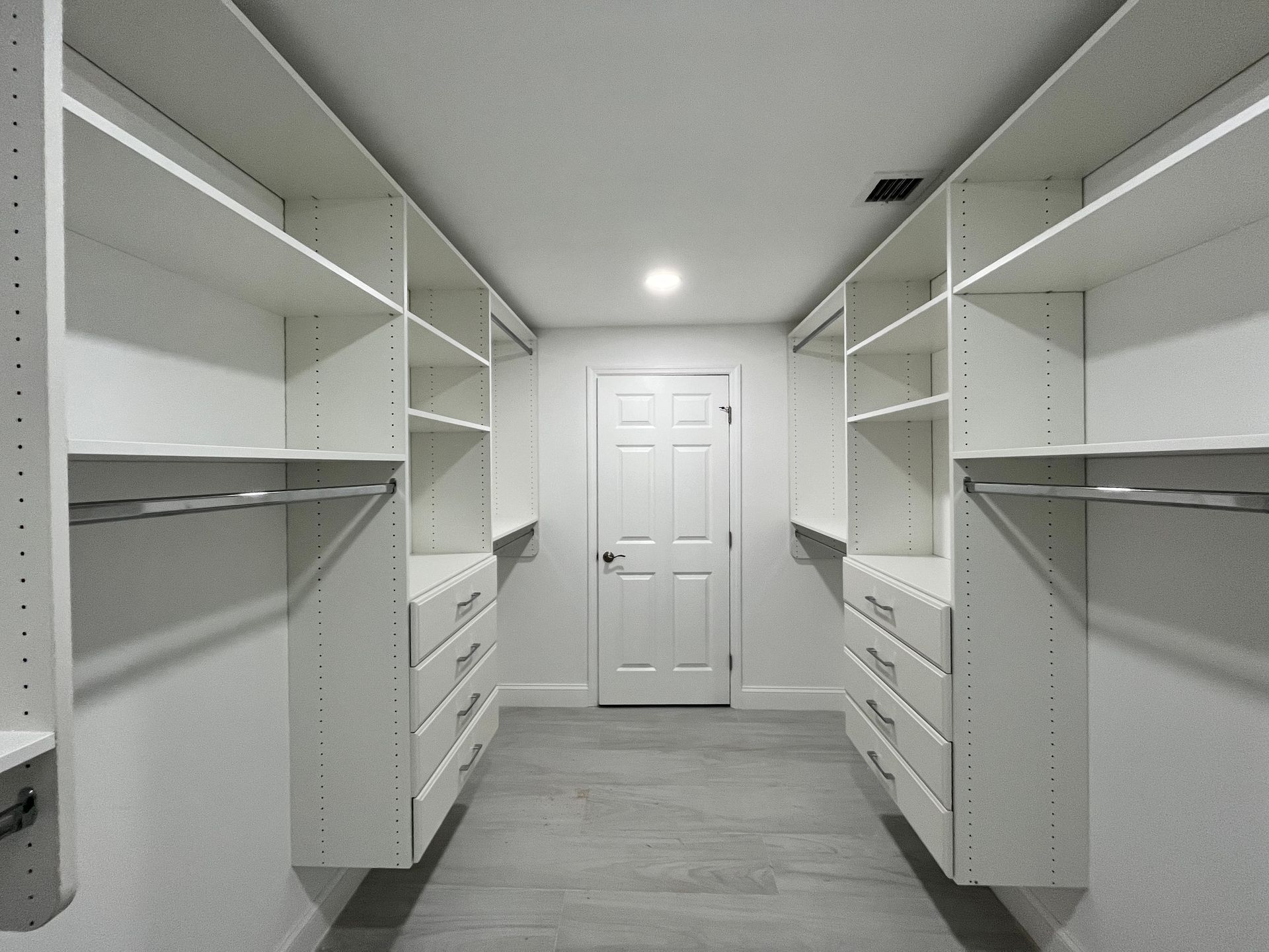 Walk-in closet with white shelves and drawers, gray carpet, and a closed white door at the end.