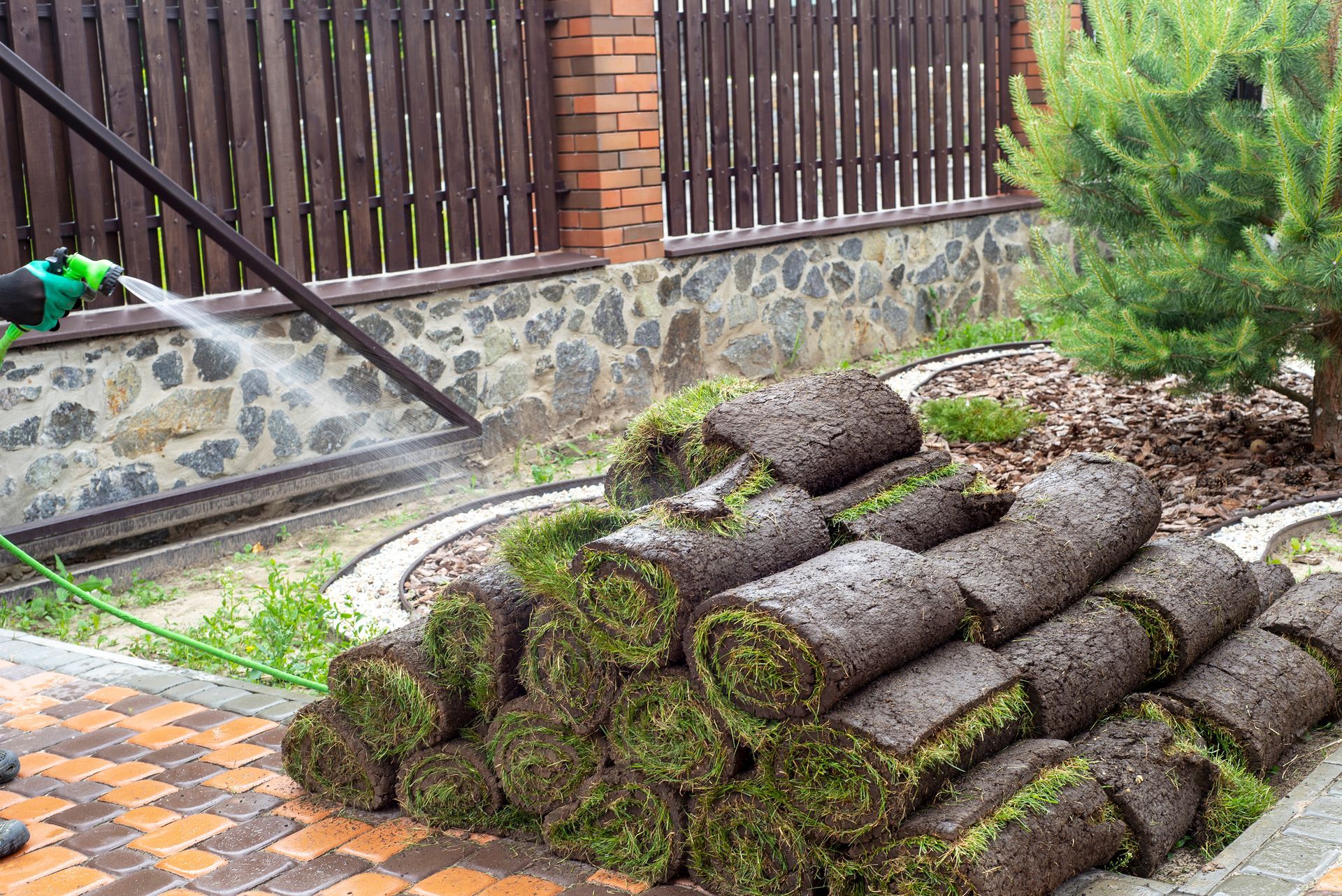 Stacked moss-covered logs in a landscaped garden beside a stone wall and wooden fence.