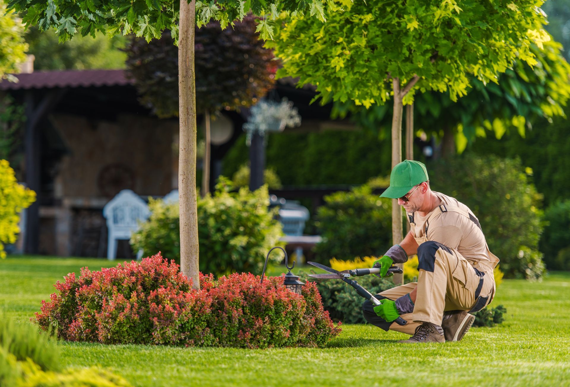 Gardener in green cap trimming a flower bed in a sunny park