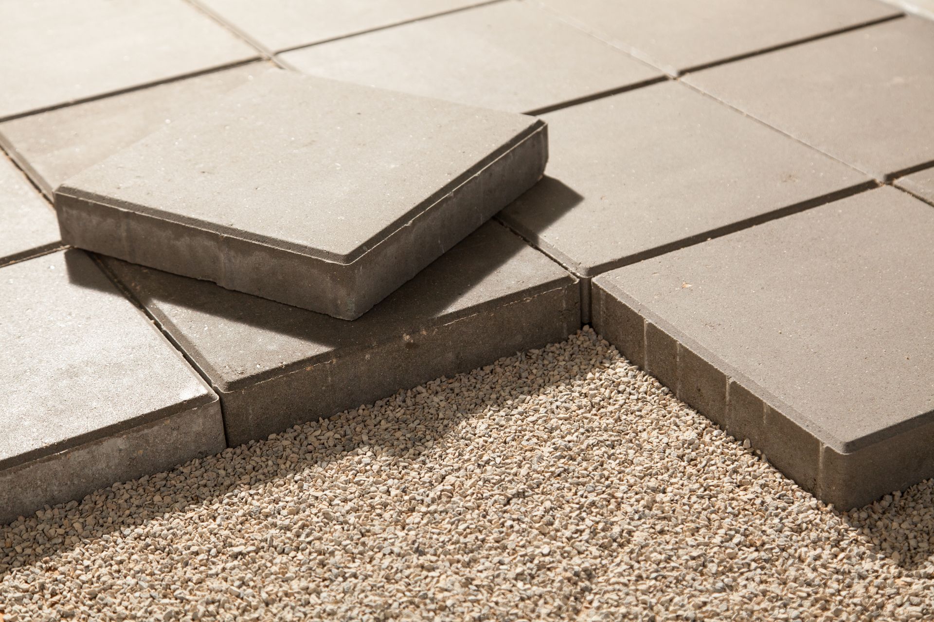 Loose concrete paving slabs over gravel with one tile lifted and misaligned