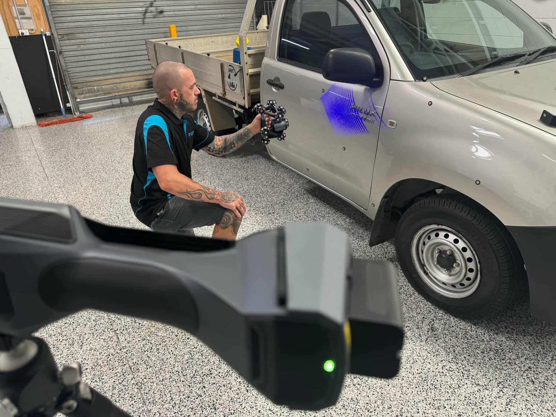 A man is kneeling down in front of a truck in a garage. — 3D Tech In Sancrox, NSW