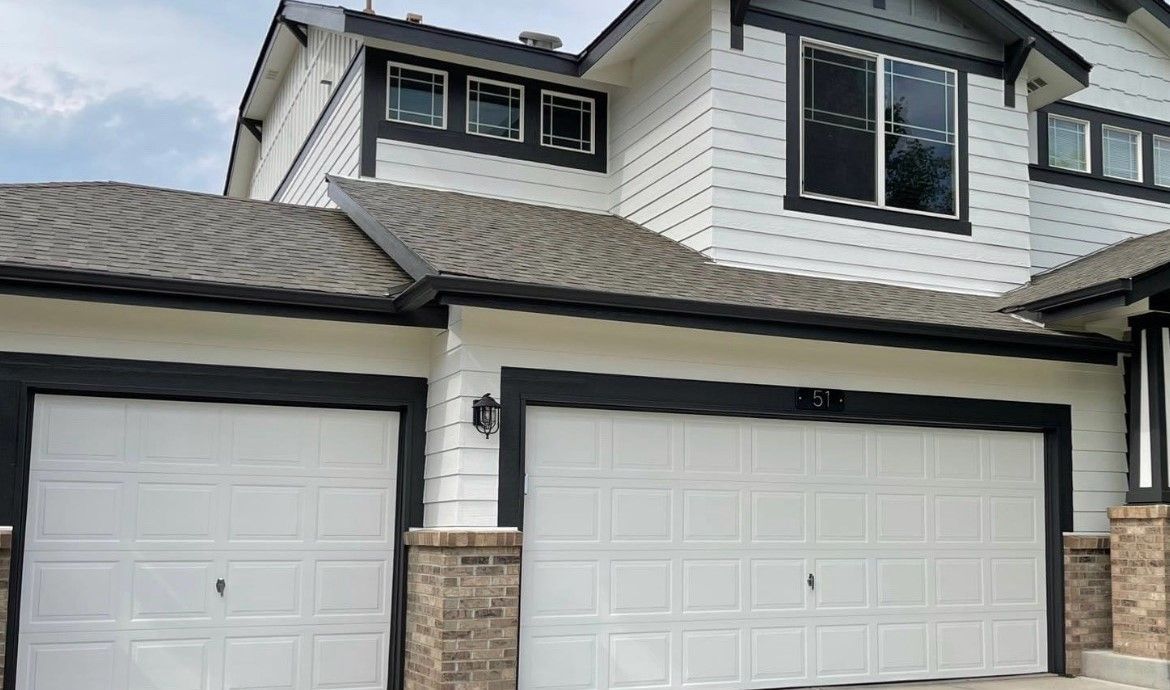 A Large White House With Two Garage Doors And A Gray Roof