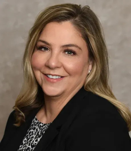 Smiling woman in a black blazer and patterned top against a neutral background
