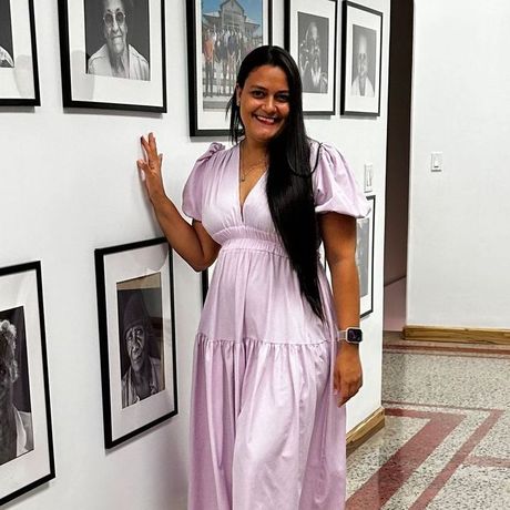 Woman in a lavender dress smiling beside framed black-and-white photos in a gallery hallway