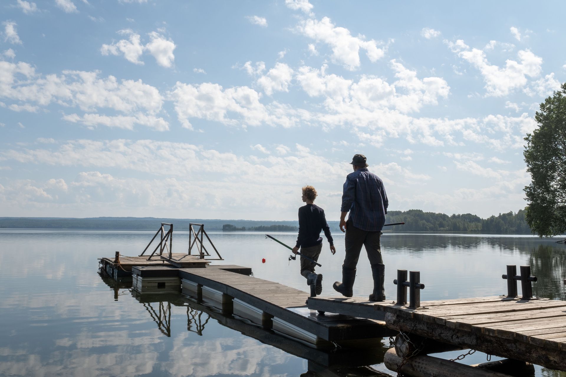 Two people on a wooden dock by a calm lake under a cloudy sky