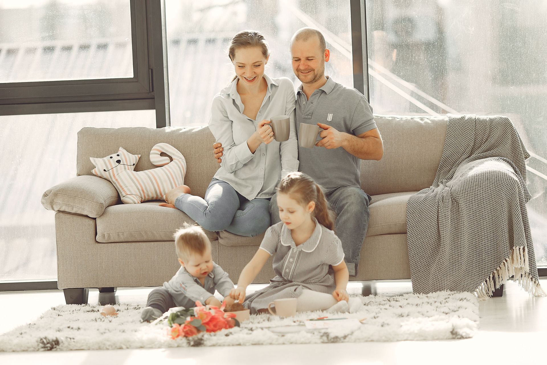 Family sitting on a couch with two children playing on a bright living room floor
