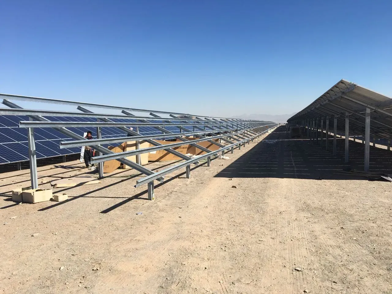 Reihen von Solarmodulen in einer Wüste, Arbeiter inspizieren die Anlage unter einem klaren blauen Himmel