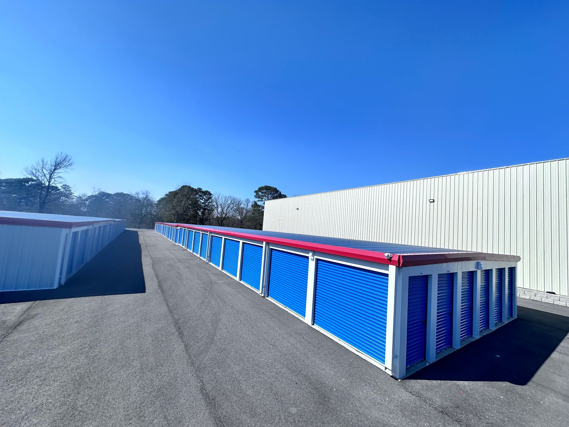 Row of blue storage units with red trim along a paved lot under a clear blue sky