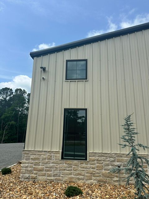 Side of beige metal building with stone base, narrow windows, and blue sky overhead.