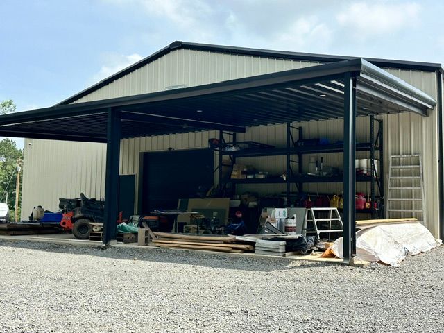 Open metal garage with equipment and tools stored inside on a gravel lot