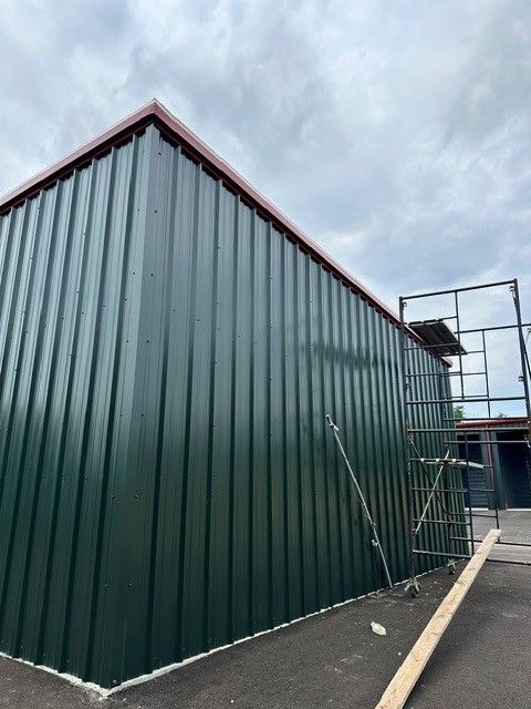 Green corrugated metal building with a red roof trim beside a narrow paved walkway