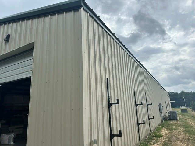 Tan metal warehouse building with a roll-up door under a cloudy sky
