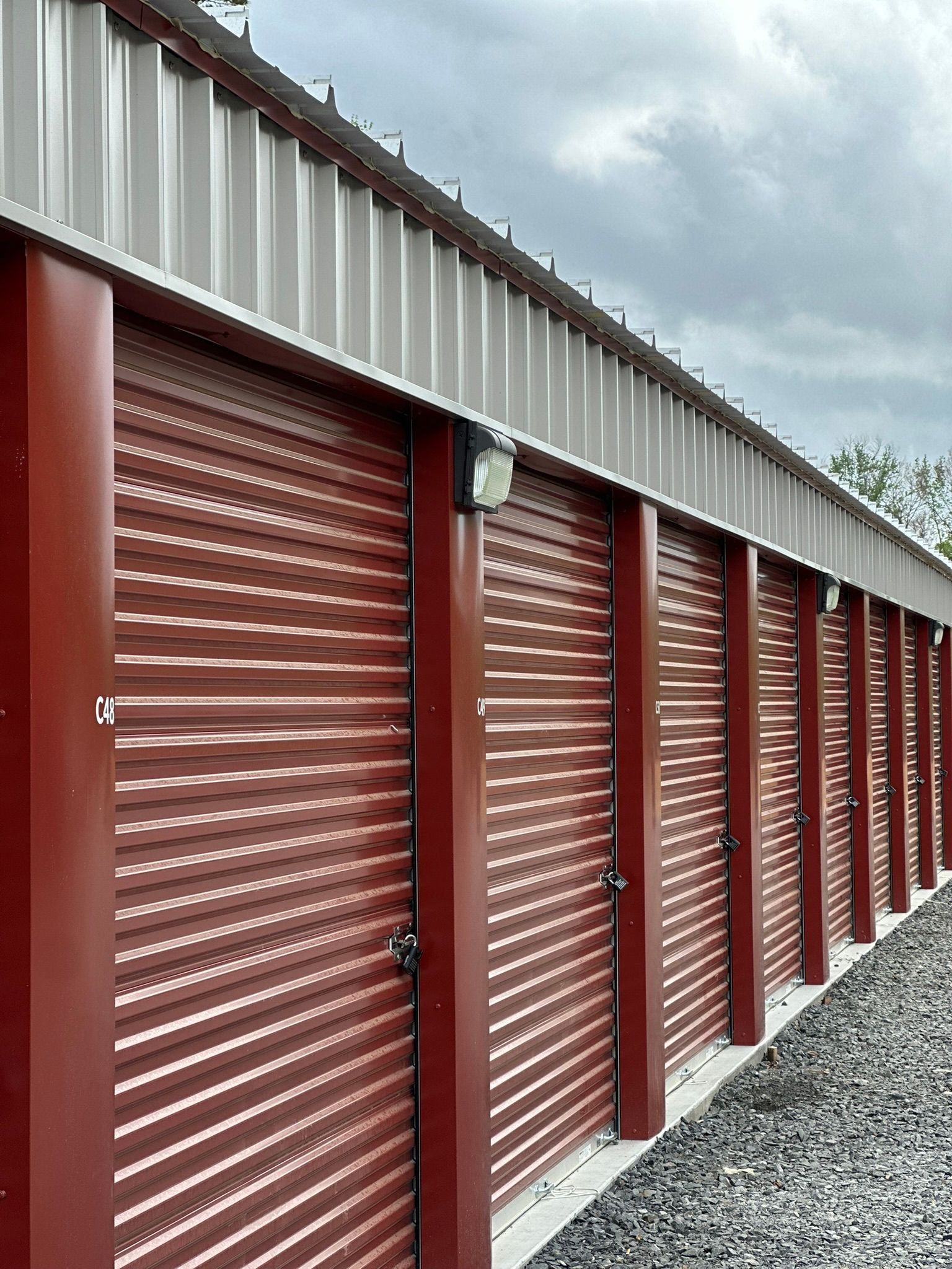 Red storage unit doors along a row of outdoor self-storage lockers with a gravel aisle