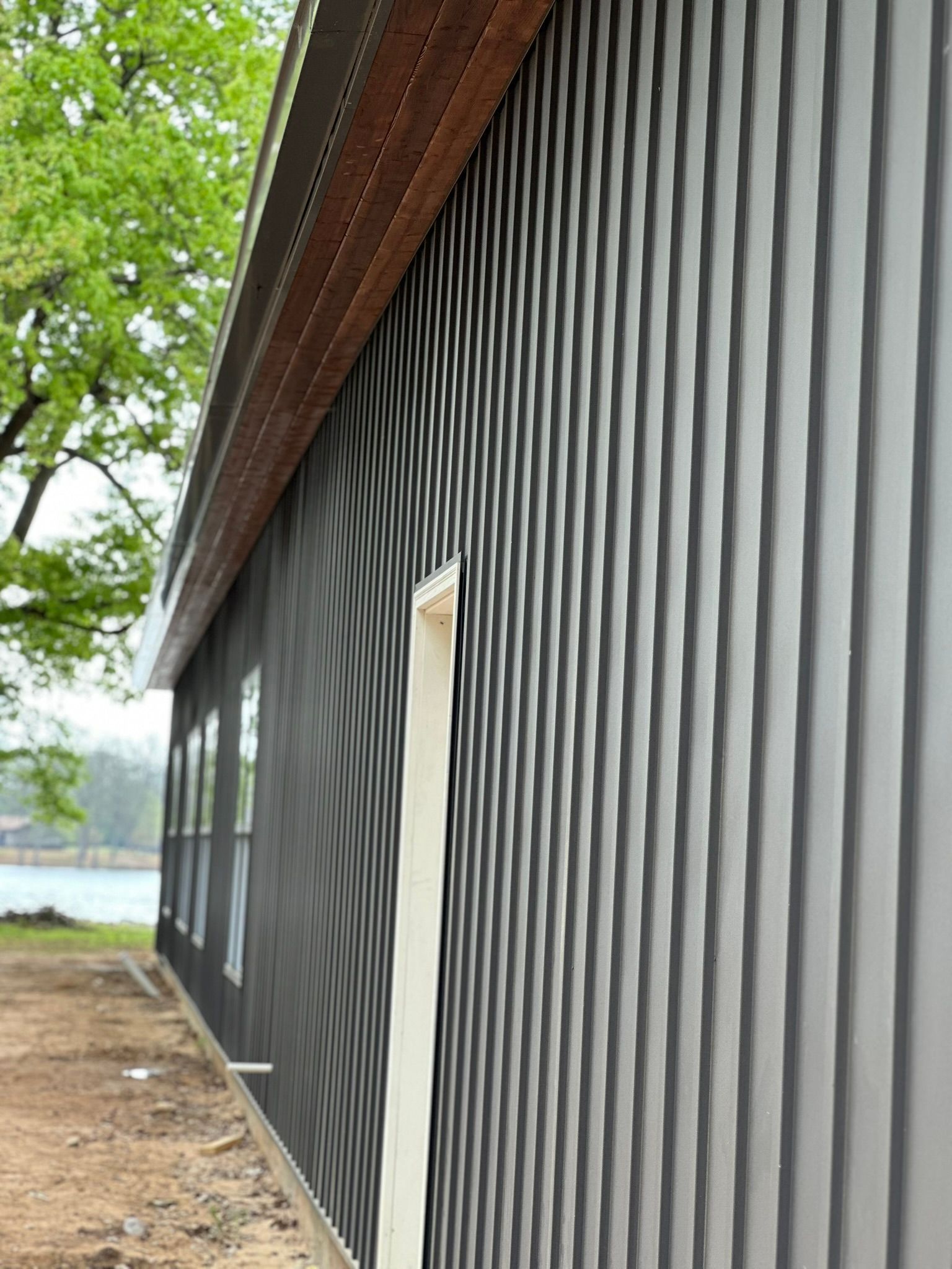 Black corrugated building exterior with a white door beside leafy trees and a dirt path